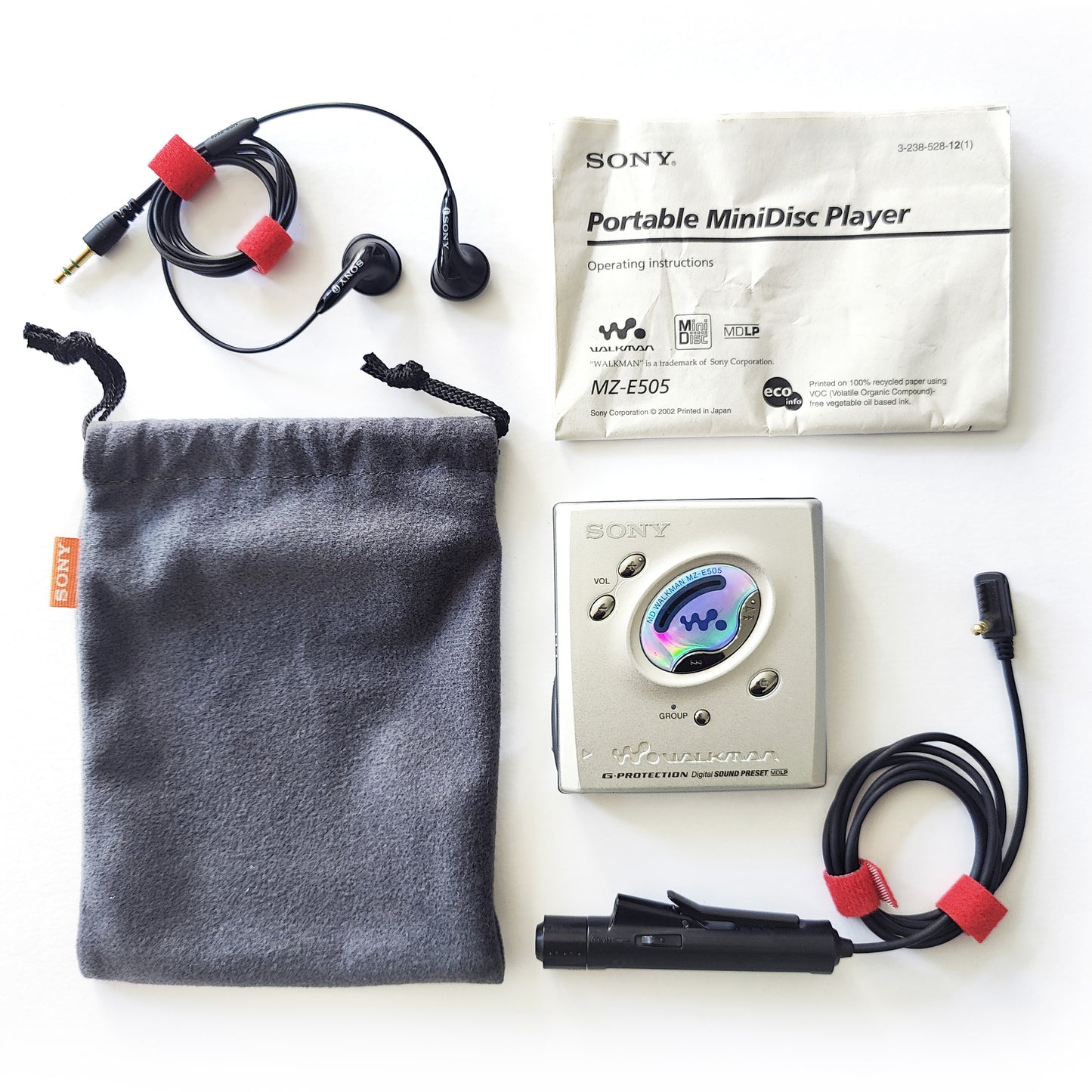 A bird's-eye view of a vintage silver Sony MZ-E505 MiniDisc player with instructions, a black Sony RM-MC11EL remote control, black Sony MDR-E808 earphones and a grey Sony branded carrying pouch neatly laid out.